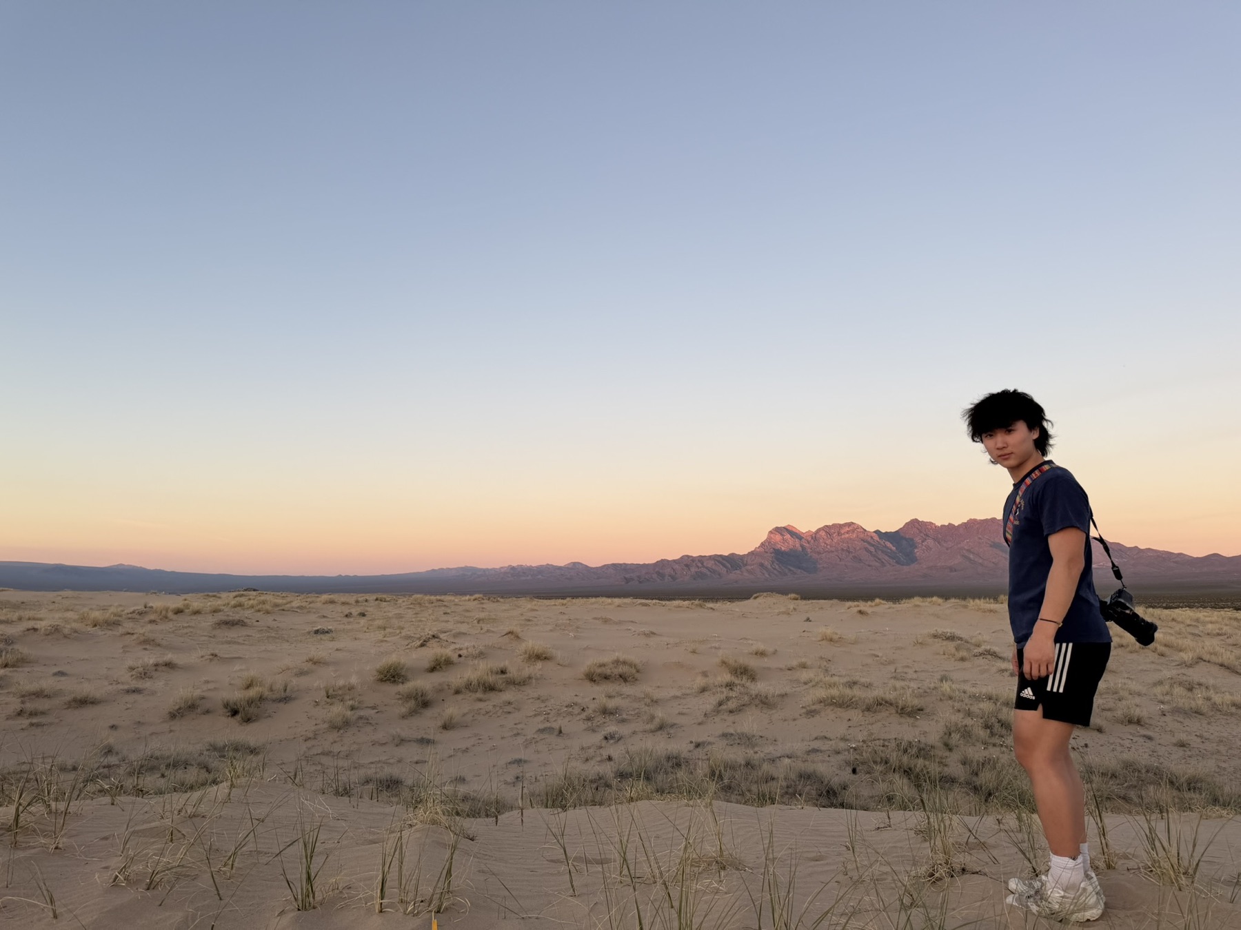 Winston standing in the desert at sunset with a camera on his shoulder, looking back toward the viewer.