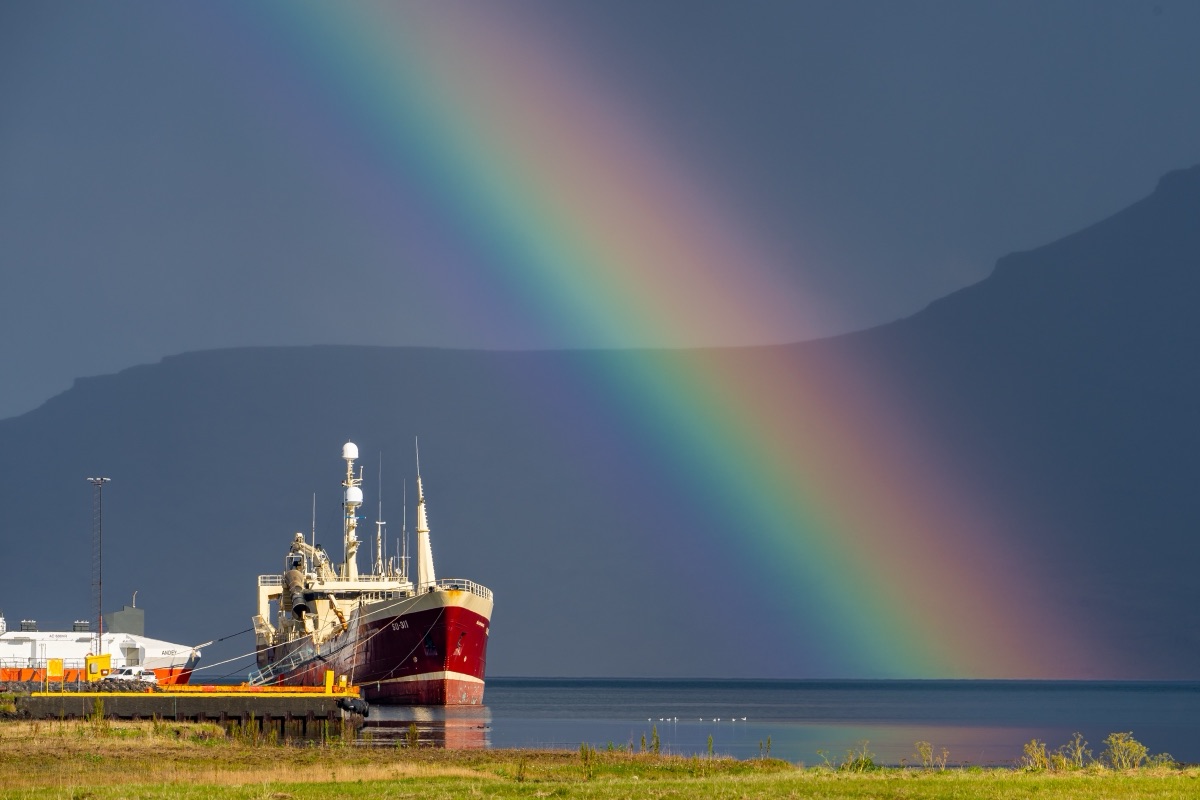 A rainbow arcing over a fishing vessel moored in an Icelandic fjord