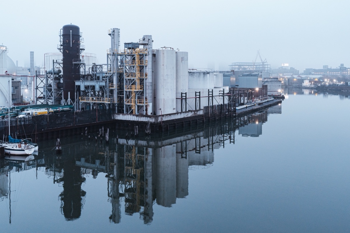 Industrial storage tanks and refinery towers reflected in still water on a foggy morning