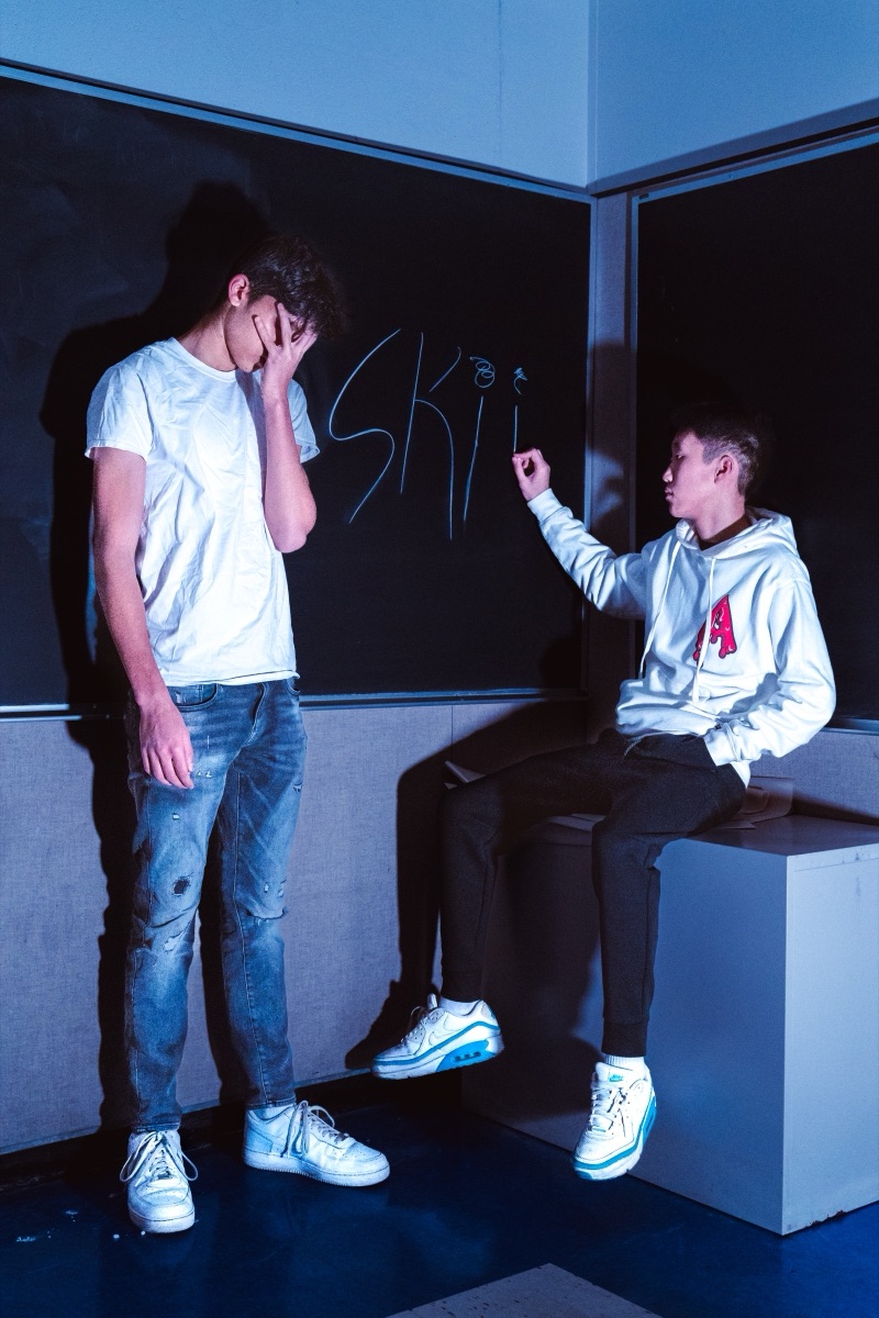 Two teenagers messing around by a chalkboard in a classroom lit by blue light