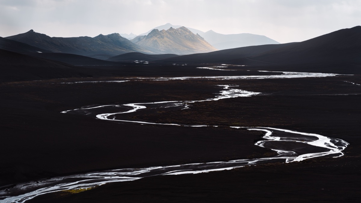 Braided glacial river threading across black volcanic sand in the Icelandic highlands