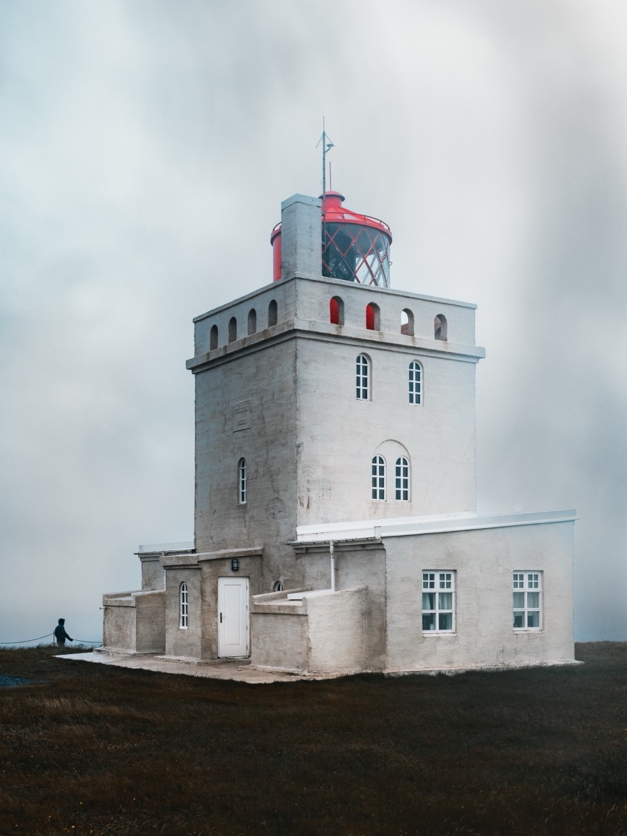 A lone visitor beside Dyrholaey lighthouse under heavy grey cloud, Iceland