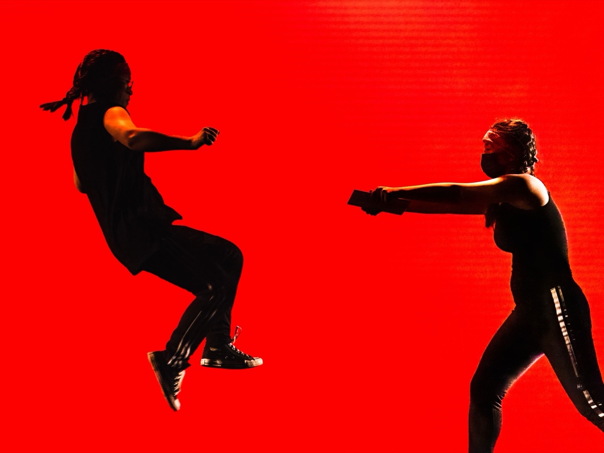 Two dancers silhouetted mid-leap against a saturated red backdrop during a stage performance