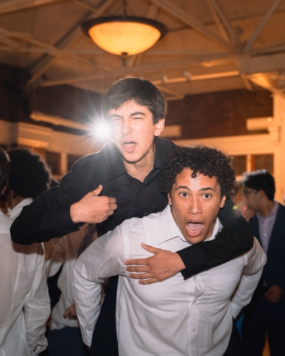 Two students clowning for the camera, one riding piggyback, at a school dance