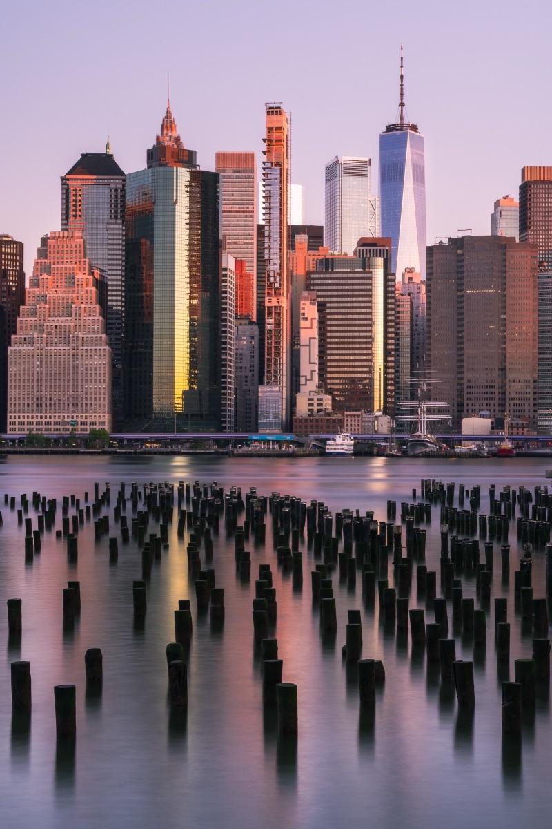 Lower Manhattan and One World Trade Center at dawn, seen across the old pier pilings in Brooklyn Bridge Park