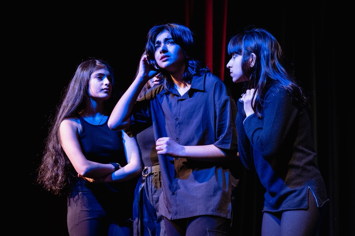 Three actors caught mid-scene under blue stage light during a theatre performance