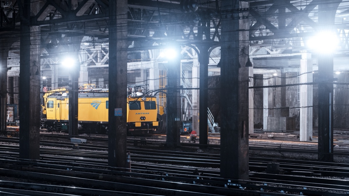 A yellow Amtrak maintenance locomotive between the columns of a floodlit rail yard at night