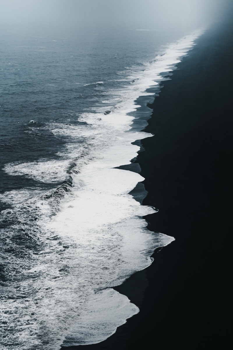 Surf breaking in a long white line along the black sand of Reynisfjara beach, Iceland