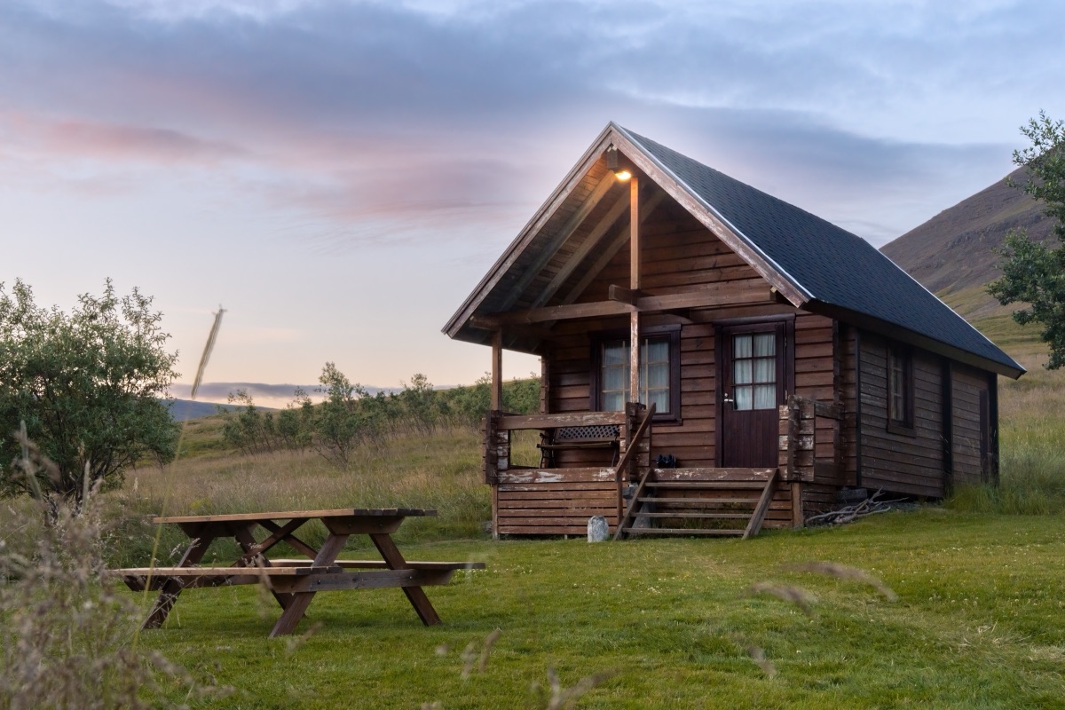 A lit wooden cabin and picnic table under a pink summer sky at midnight, Iceland