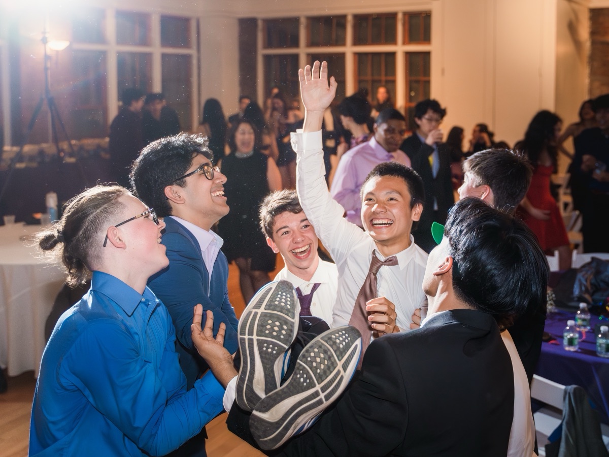 Students laughing as a friend is lifted overhead on the dance floor at a school formal