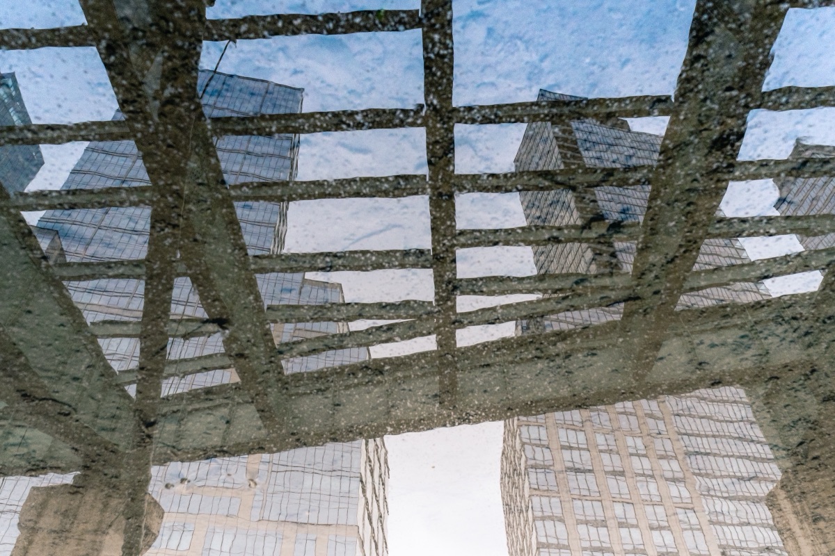 Skyscrapers mirrored in a rain puddle on a city sidewalk, reflection inverted