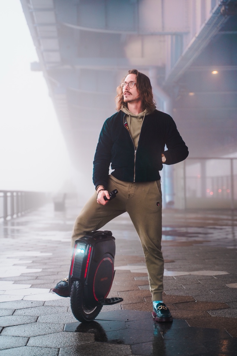A rider standing with his electric unicycle under an elevated roadway in heavy fog