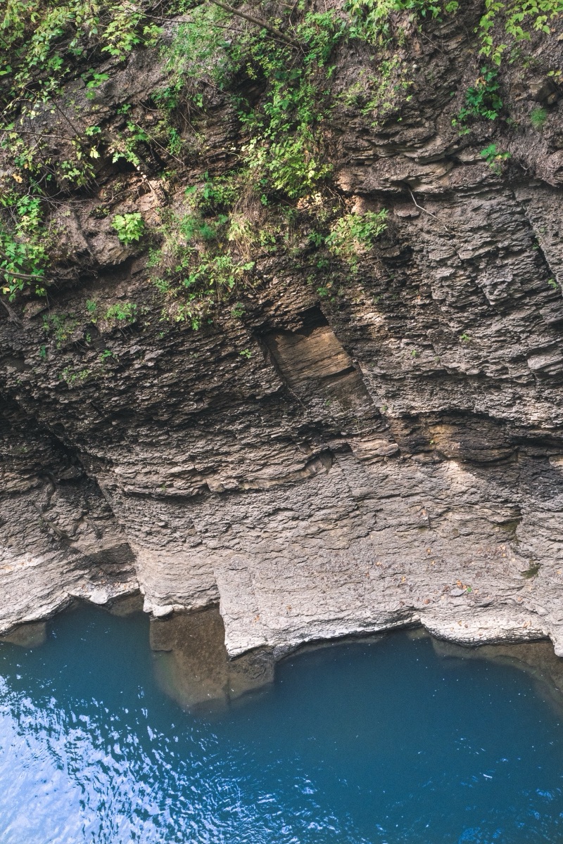 Layered shale cliffs dropping into a still blue-green plunge pool, Finger Lakes, New York