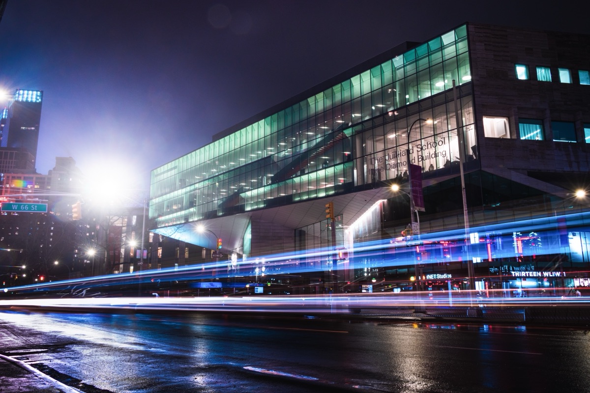 Traffic light trails streaking past the glass facade of the Javits Center at night, New York