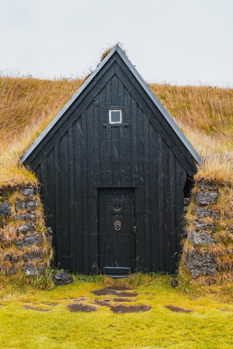A black timber chapel set into a turf-walled bank, Iceland