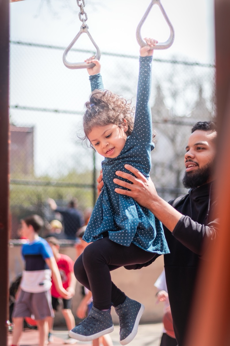 A father lifting his daughter across the playground rings on a spring afternoon